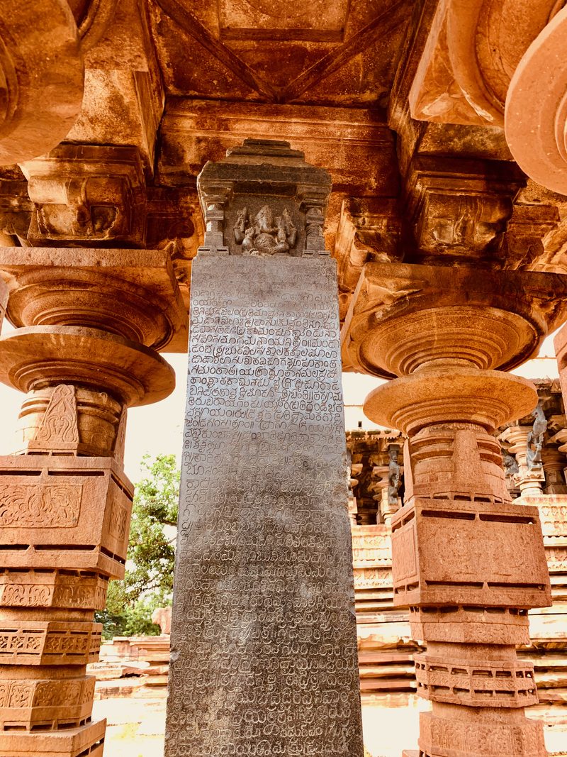 One face of the black inscription pillar shows a small carving of Ganesa at the top and close rows of letters below it.