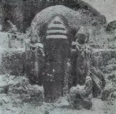 A grainy photograph of a carved stone in an arched niche, topped by three stacked umbrella-like tiers, with small statues on both sides.