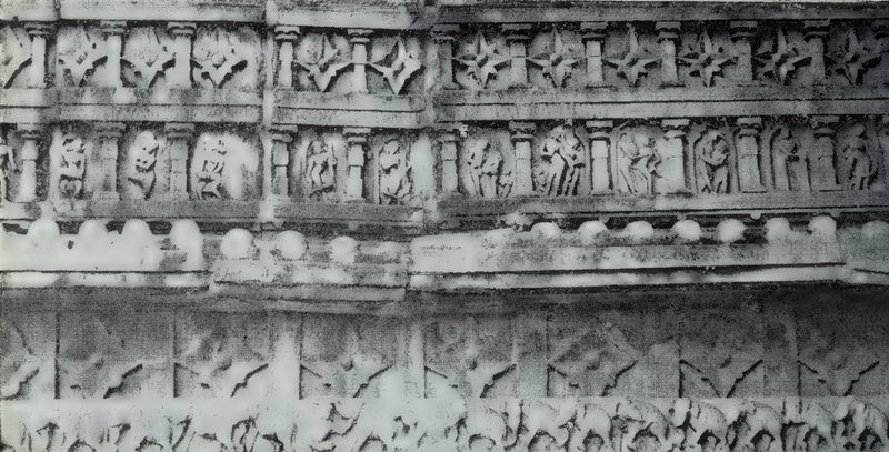 A close view of a carved stone wall in horizontal bands, with rows of small statues and star-shaped motifs above and a row of elephants along the bottom.