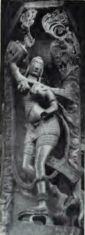 A bracket sculpture of a woman among carved scrolls and small attendant statues, on a pillar.
