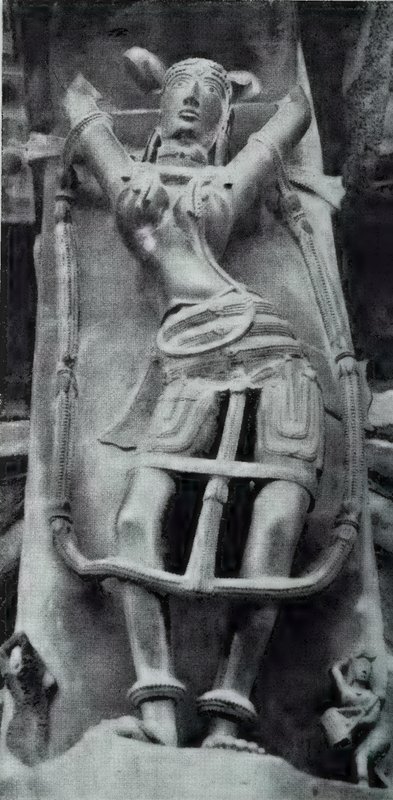 A bracket sculpture of a woman with her arms raised, framed by a long curved band, with small statues at her feet.