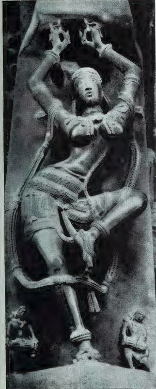 A bracket sculpture of a dancing woman with both hands raised above her head and one leg lifted, with small statues at her feet.