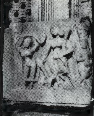 A small carved panel from a door jamb with three people carved in relief, framed by dark stone.