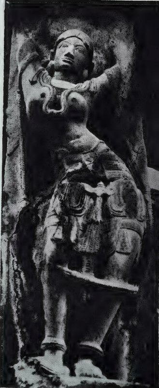 A bracket sculpture of a woman with one arm raised behind her head, carved on a dark stone pillar.