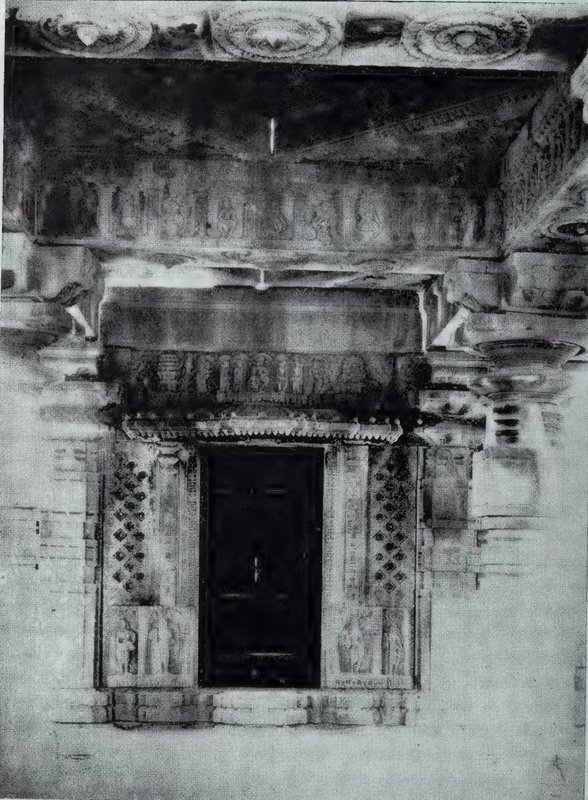 A temple doorway with a dark door, carved lattice panels on each side, and carved bands on the lintel and eave above.