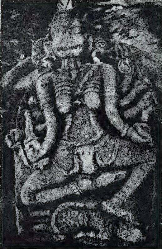A seated goddess with many arms and a gaunt face, carved in stone, with one leg folded across the other.