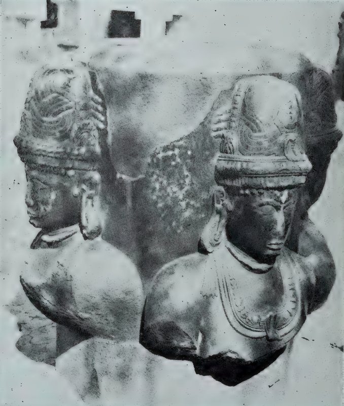A close view of a stone linga with crowned faces carved on its sides. Two faces are visible.