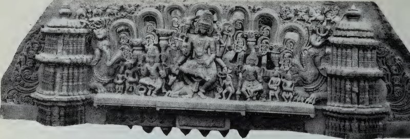 A long carved stone architrave with a large central statue among many small statues under arches, between two tower-shaped ends.