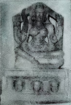 A faded photograph of a small seated goddess carved on a stone slab with a pointed top, on a pedestal with three round carved motifs.
