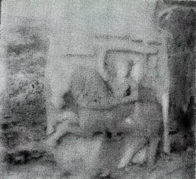 A blurred photograph of a carved hero-stone with a man and a large animal.