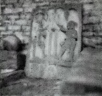 A blurred photograph of a carved slab with standing people, set against a brick wall.