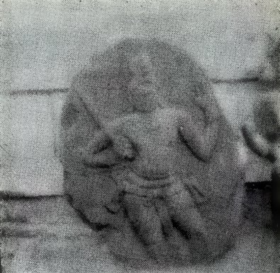 A blurred photograph of a rounded carved stone with a seated person.