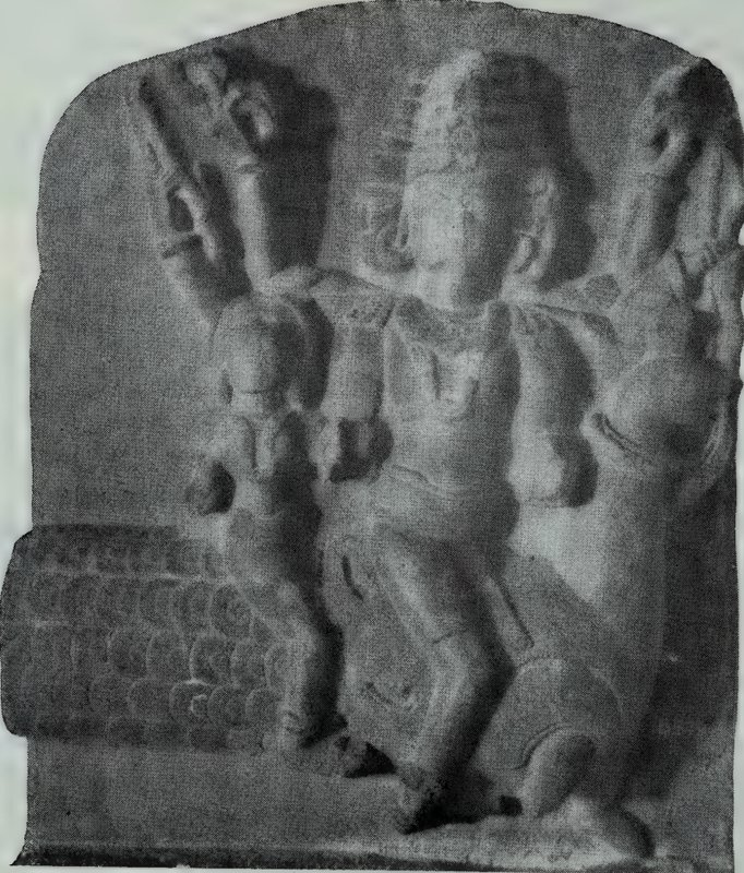 A stone relief of a seated god with several heads and many arms, on a stele with a rounded top.