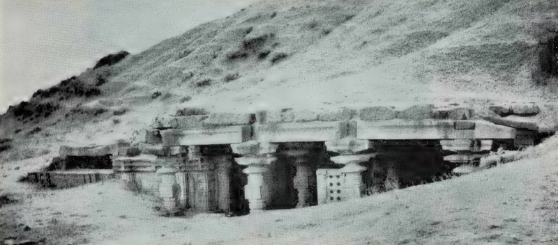 A small temple partly buried in the slope of an earthen rampart, with its pillars and lintels visible.