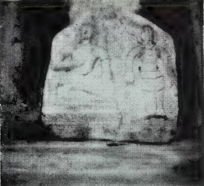 A blurred relief of two seated people on a stone slab, in a dark recess.