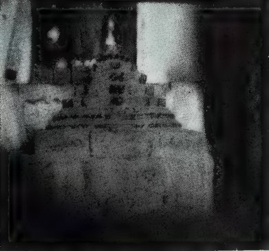 A dark photograph of a stepped, pyramid-shaped stone object on a base, inside a dark shrine.