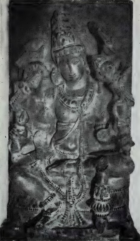 A worn stone statue of a crowned deity wearing heavy necklaces, carved on a dark slab.