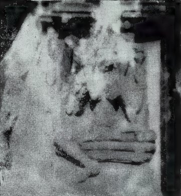 A grainy, high-contrast photograph of a damaged stone statue under a carved canopy. The details are hard to make out.