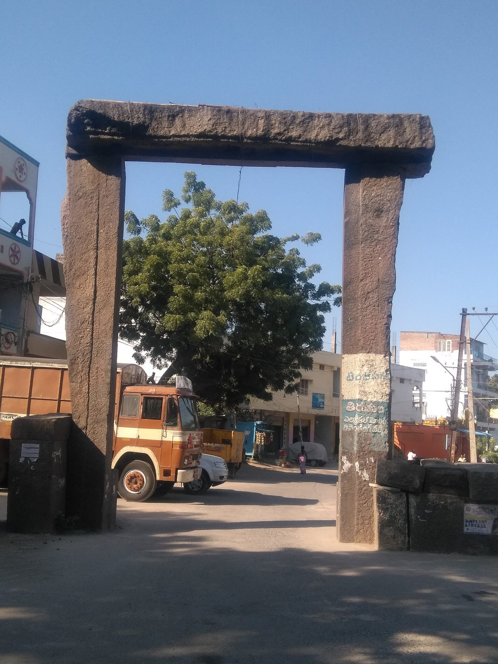 హనమకొండ వద్ద ఒక ఎత్తైన రాతి ద్వారం. రెండు కఠినమైన ఏకశిలా స్తంభాలు ఒకే భారీ రాతి లింటెల్ను కలిగి ఉంటాయి, మరియు ట్రక్కులు మరియు భవనాలతో కూడిన వీధి దాటి ఉంటుంది.