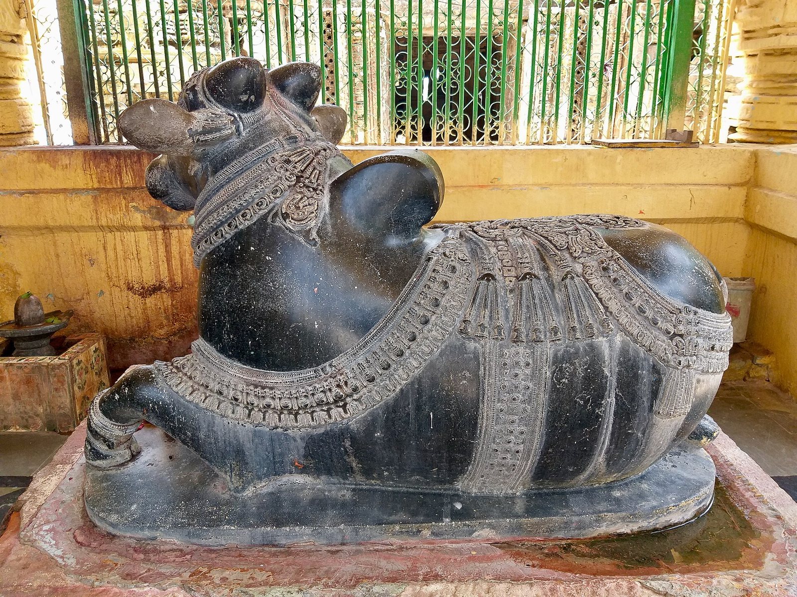 A large black polished stone bull lies on a pedestal. Its harness and bells are carved in detail.
