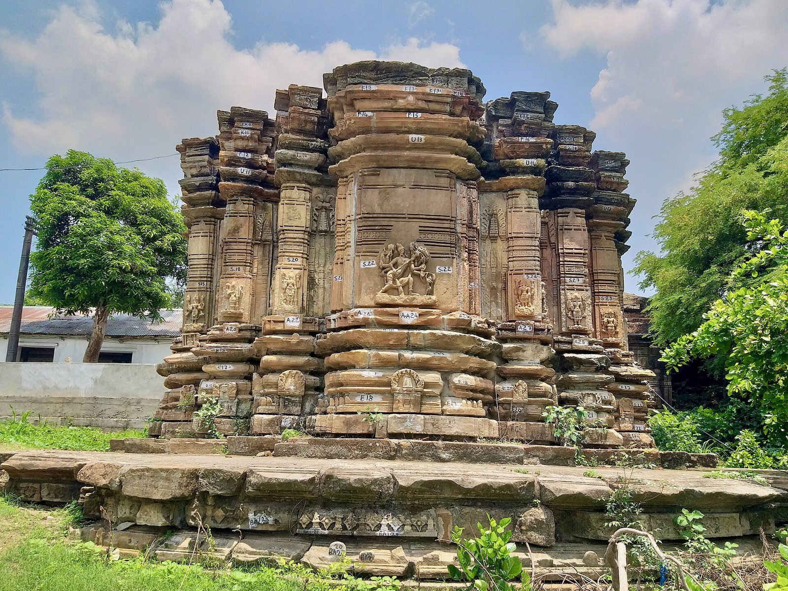 A broad temple base of many projecting stone layers, with carved niches and pillasters, stands on a low platform under a blue sky.