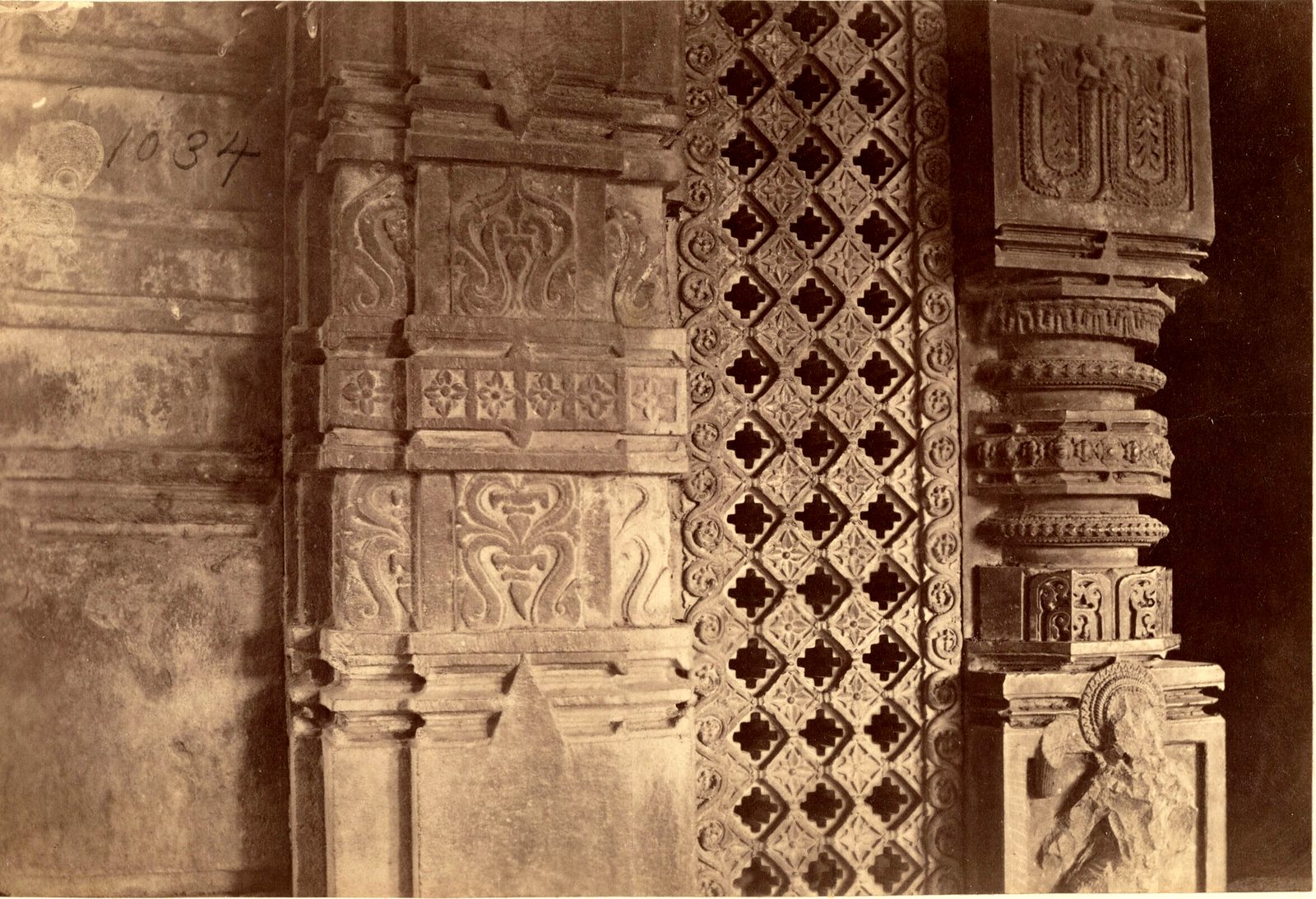 Close view of a carved door jamb, a pierced stone screen with a lattice of cross shapes, and a carved pillar. The number 1034 is written on the print.