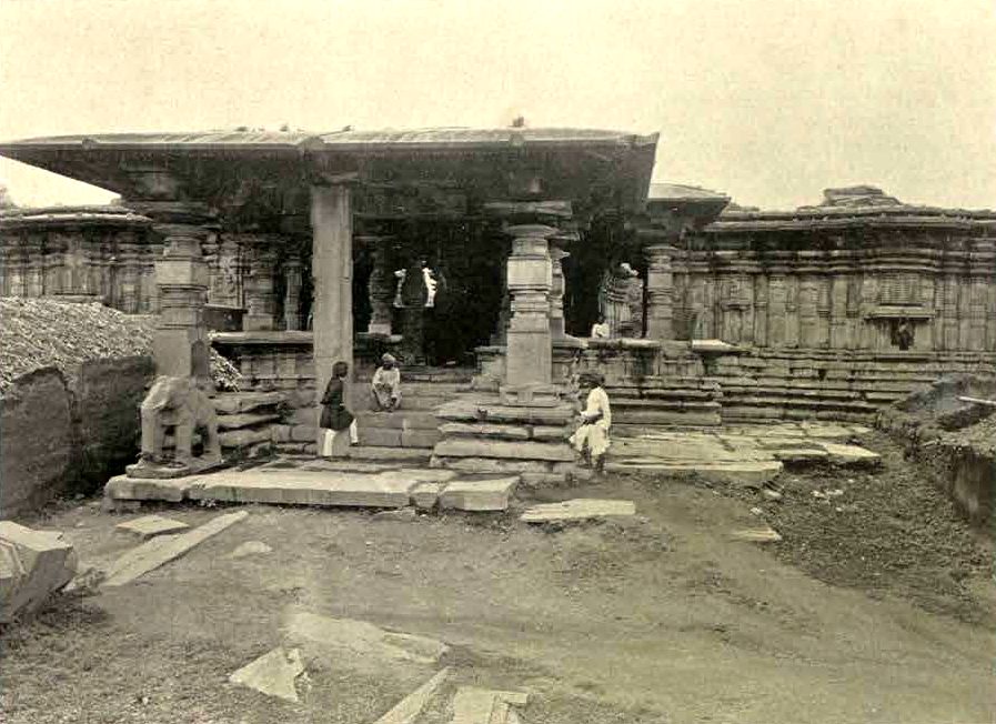 The entrance porch of the Thousand Pillar Temple, with a flat stone roof on carved pillars. A stone elephant stands at the left of the steps. Several men stand and sit on the steps, and loose slabs lie on the ground.