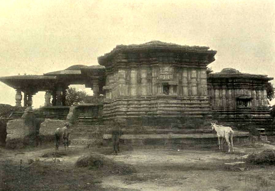 The square stone shrines of the Thousand Pillar Temple rise behind a low earth bank. A flat-roofed porch stands at the left. Two horses graze on the open ground in front.