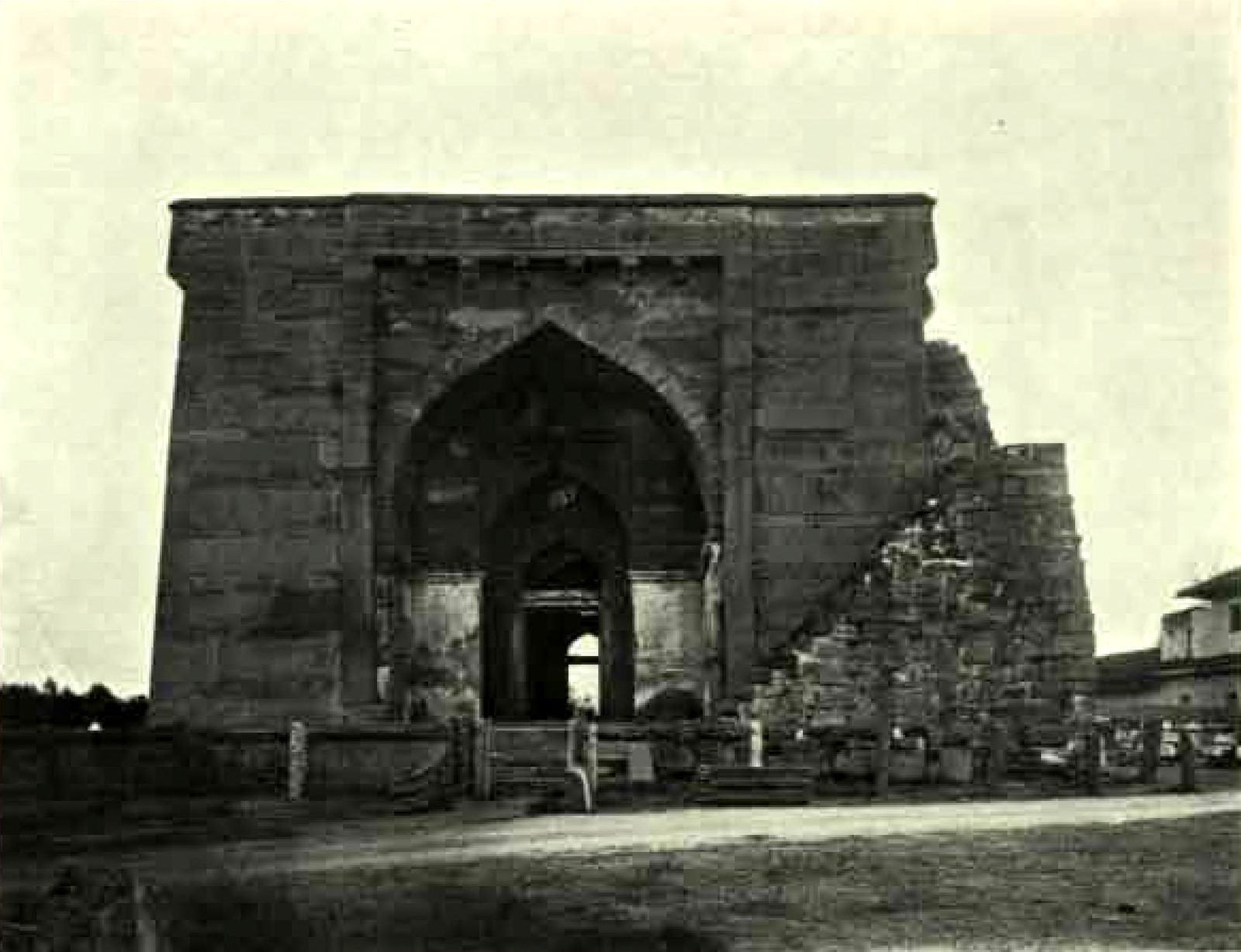 The tall, flat-topped stone front of the Khush Mahal with a deep pointed arch at its centre. A sloping mass of rough masonry leans against its right side.