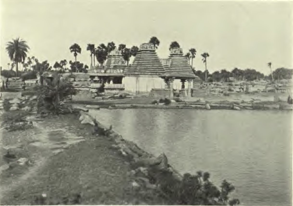 Three stepped pyramidal towers with ornamented tops rise behind a pillared porch. A pool of still water and a rough bank lie in front, with palm trees behind.