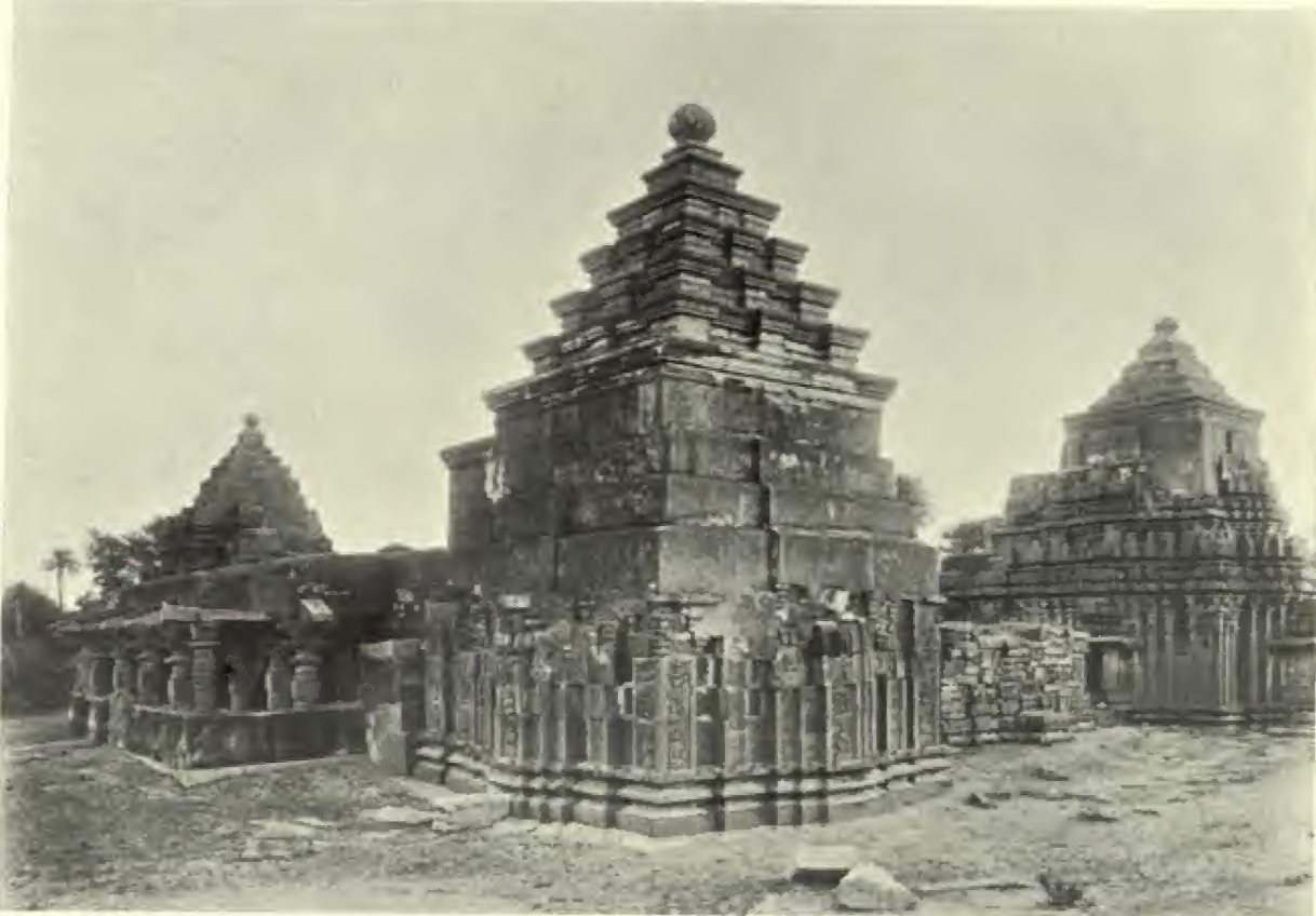 A shrine with richly carved lower walls carries a plain stepped stone tower. A second shrine with a carved tower stands to the right, and a pillared hall to the left.