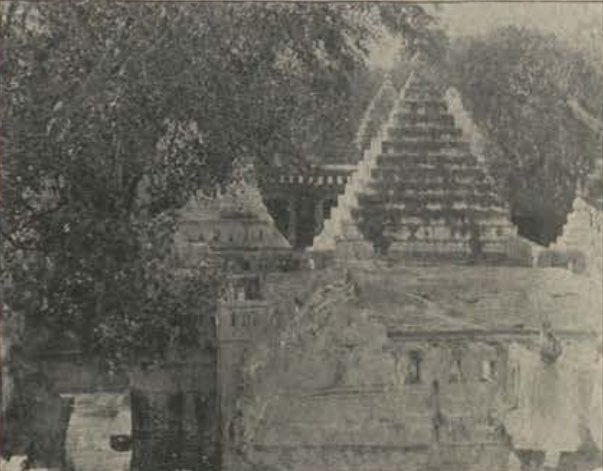 Several stepped stone temple towers rise behind a long hall with a flat roof, partly hidden by trees.