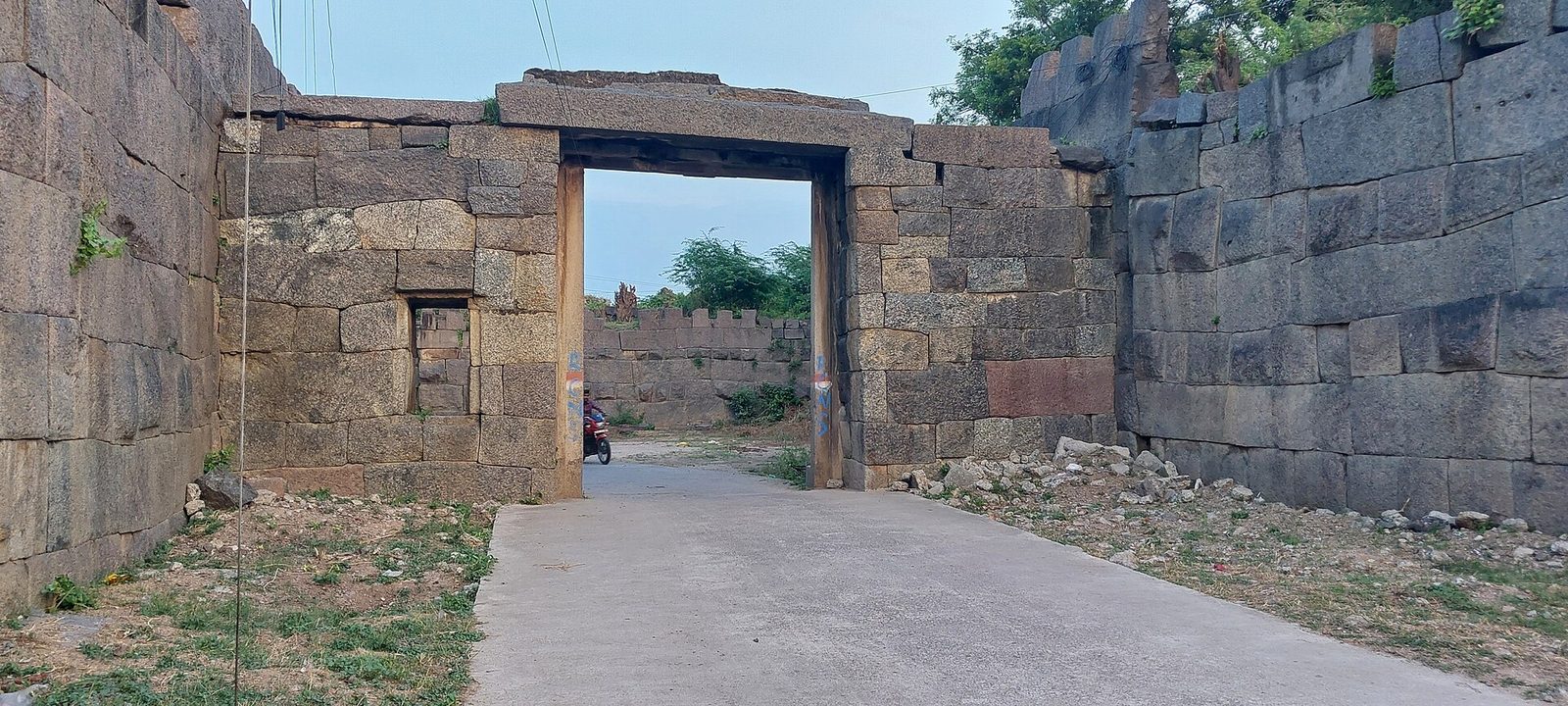 A road passing through a flat-lintelled gateway in the stone wall of Warangal Fort, flanked by walls of large dressed stone blocks